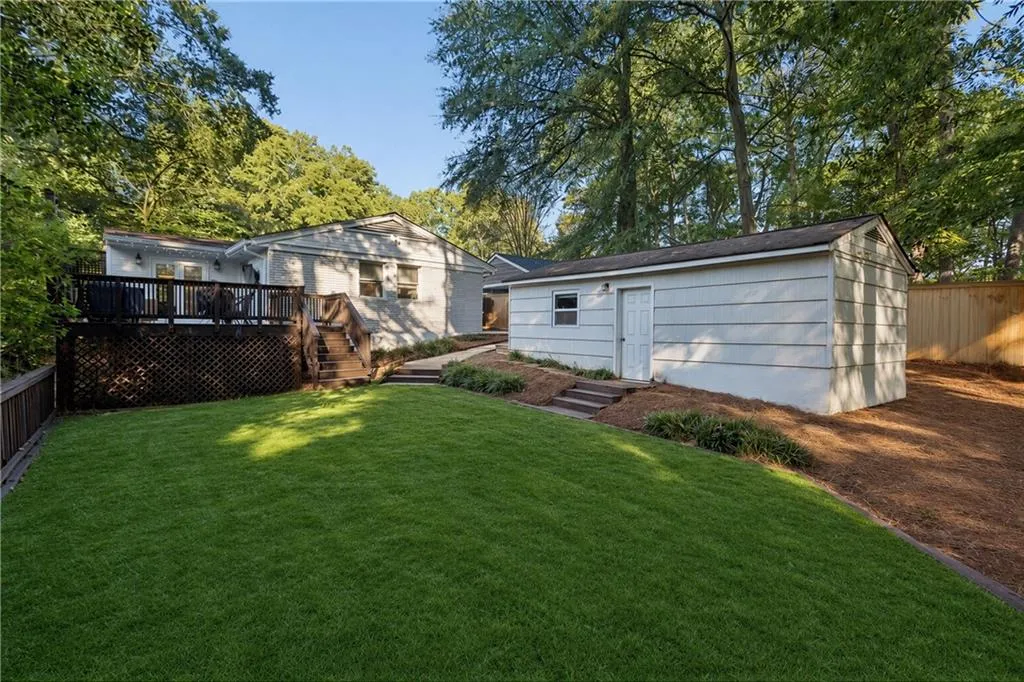 Backyard featuring a manicured lawn, elevated wood deck with lattice skirting, detached storage structure, and mature trees