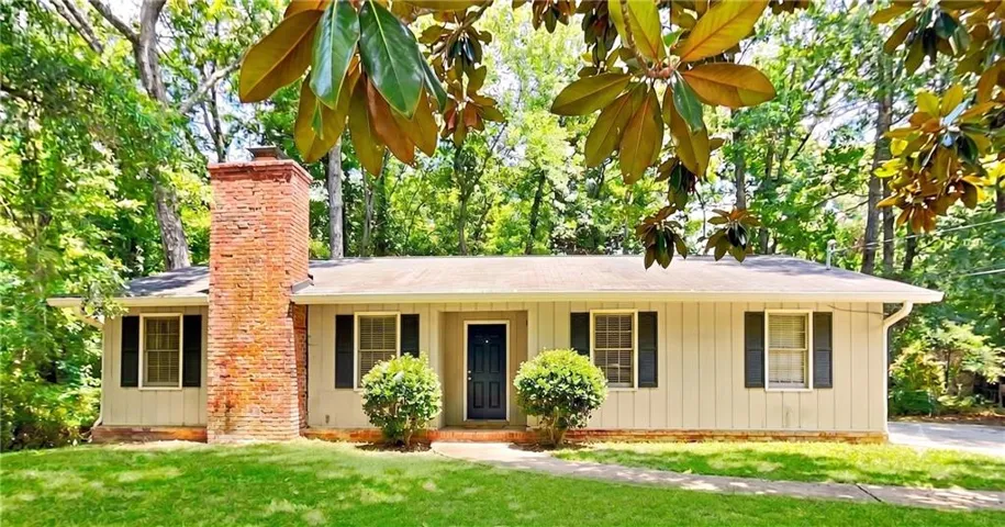 Exterior facade featuring a prominent brick chimney, light-colored siding, dark shutters, a dark front door, and a verdant front lawn