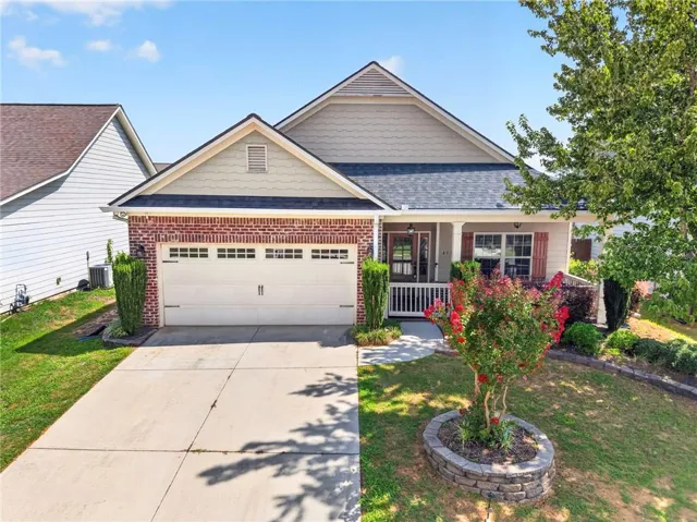 Single-story residence featuring a brick and siding facade, an attached garage, a covered front porch, a concrete driveway, and established landscaping