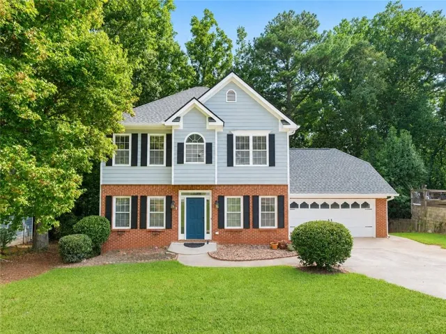 Two-story residence featuring brick and siding facade, a vibrant blue entry door, and a two-car garage with decorative window inserts