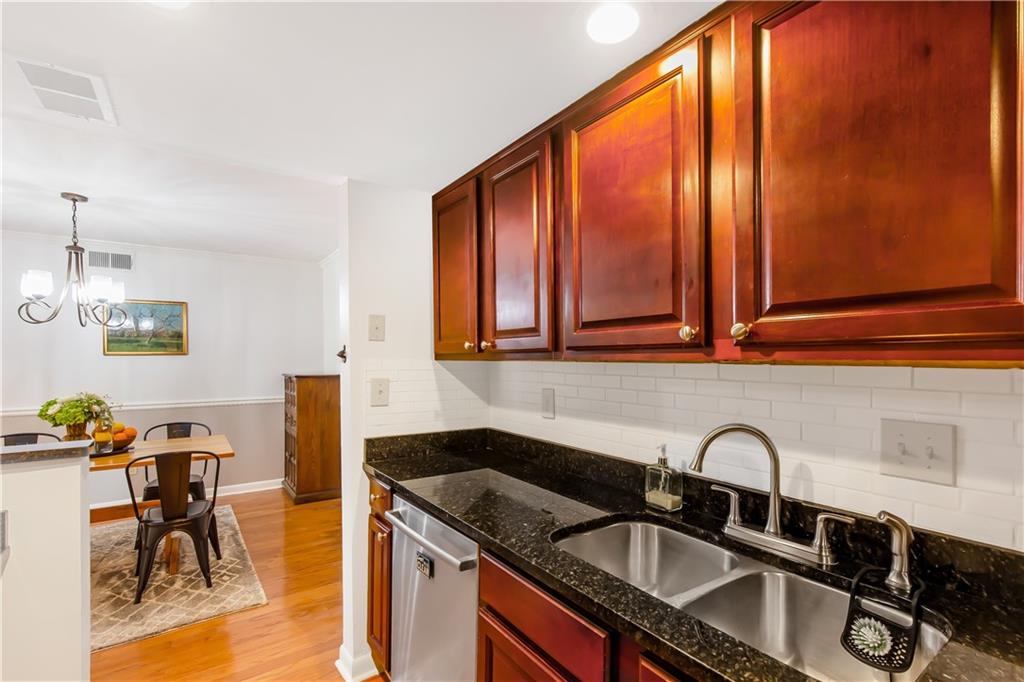 Kitchen with light wood-type flooring, an inviting chandelier, tasteful backsplash, pendant lighting, and stainless steel dishwasher