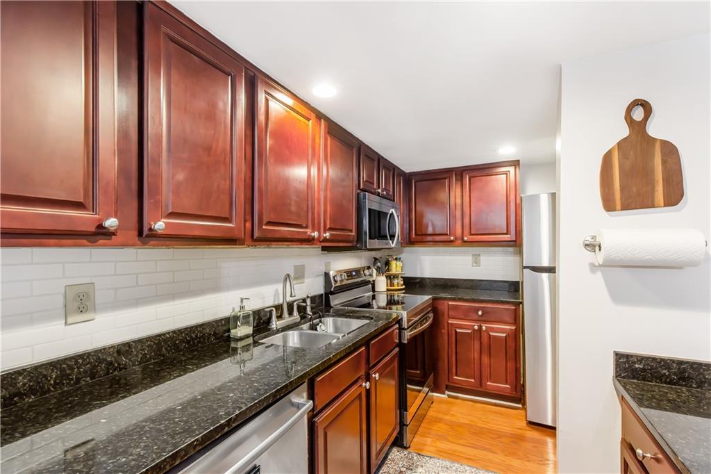 Kitchen with dark stone counters, tasteful backsplash, appliances with stainless steel finishes, light hardwood / wood-style floors, and sink