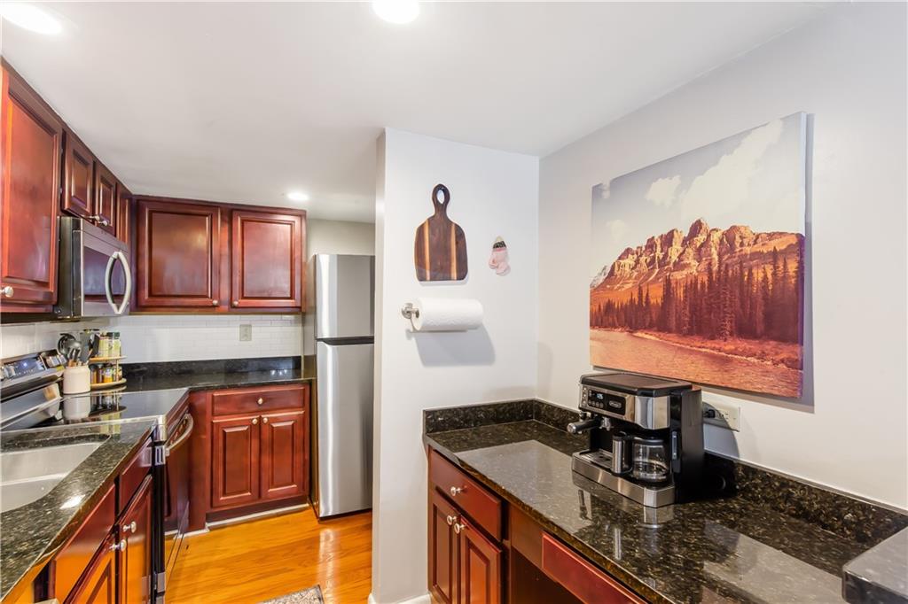 Kitchen with light wood-type flooring, tasteful backsplash, stainless steel appliances, and dark stone counters