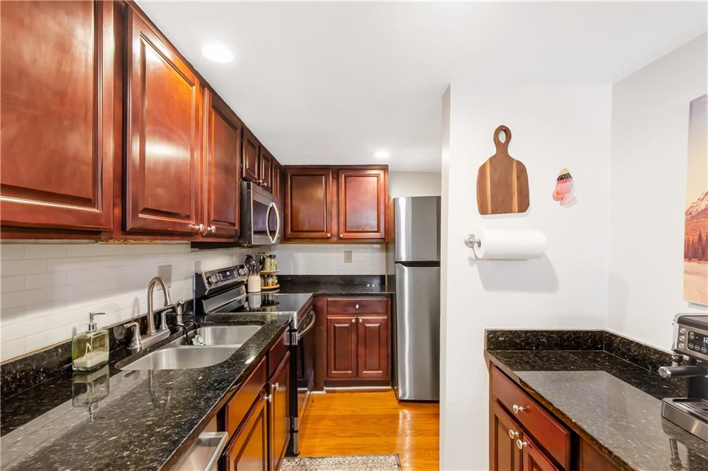 Kitchen with tasteful backsplash, light hardwood / wood-style floors, stainless steel appliances, and dark stone countertops
