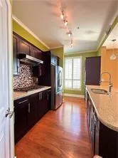 Kitchen with crown molding, light stone counters, light wood-type flooring, stainless steel appliances, and dark wood finish cabinets
