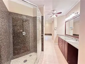 Full bathroom with light tile patterned floors, double vanity, ceiling fan, a shower stall, and ornamental molding