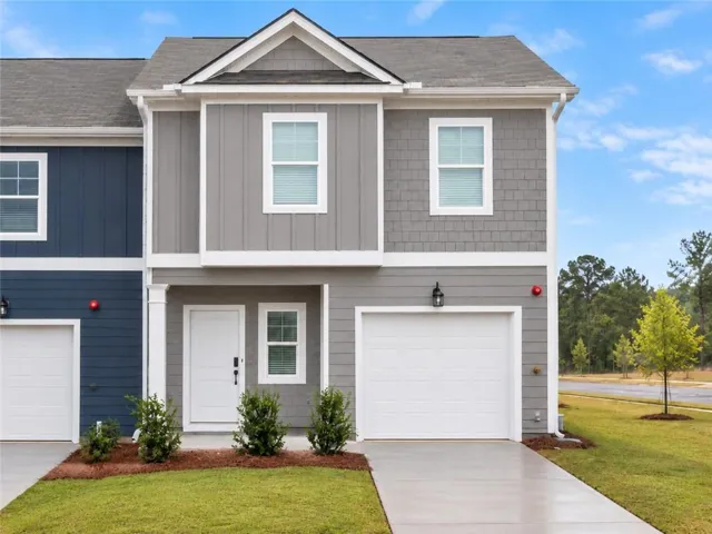 Contemporary townhome facade with mixed material siding, an integrated garage, a white entry door, and manicured landscaping
