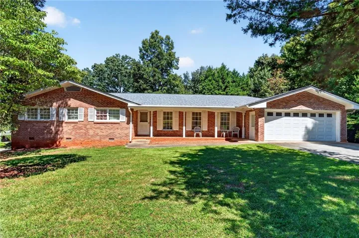 Brick exterior with white shutters, a covered front porch, and an attached two-car garage
