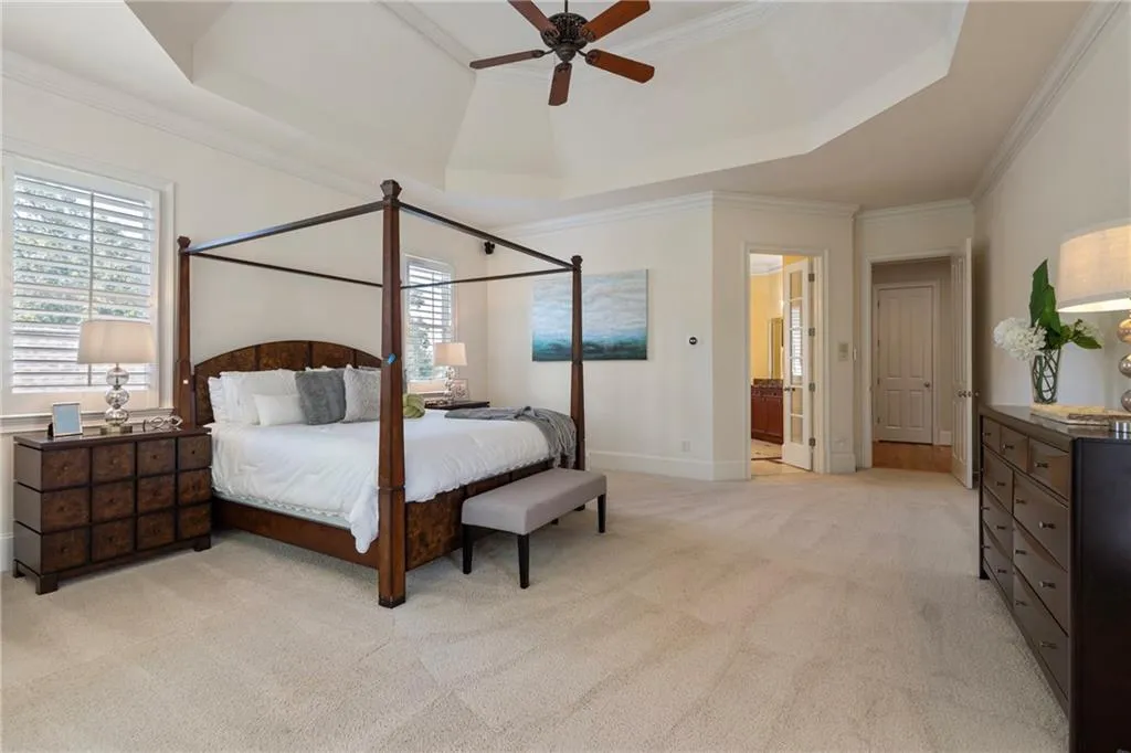 Bedroom with a raised ceiling, ornamental molding, light carpet, and multiple windows
