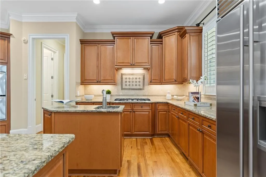 Kitchen with high quality fridge, light wood-type flooring, ornamental molding, light stone countertops, and a center island