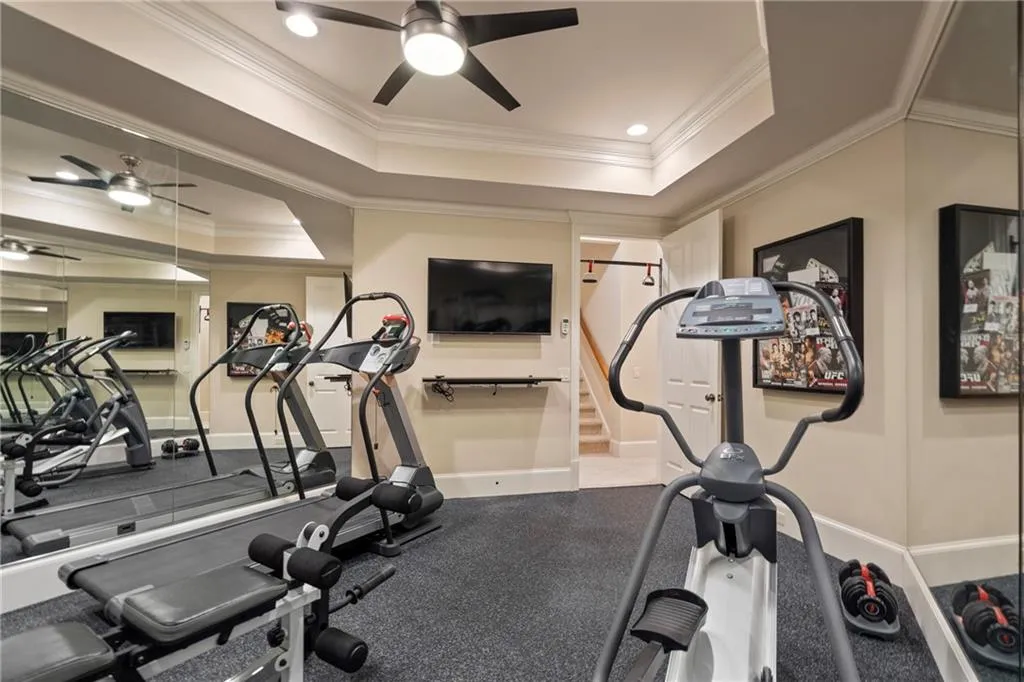 Exercise room with a ceiling fan, a tray ceiling, ornamental molding, and recessed lighting