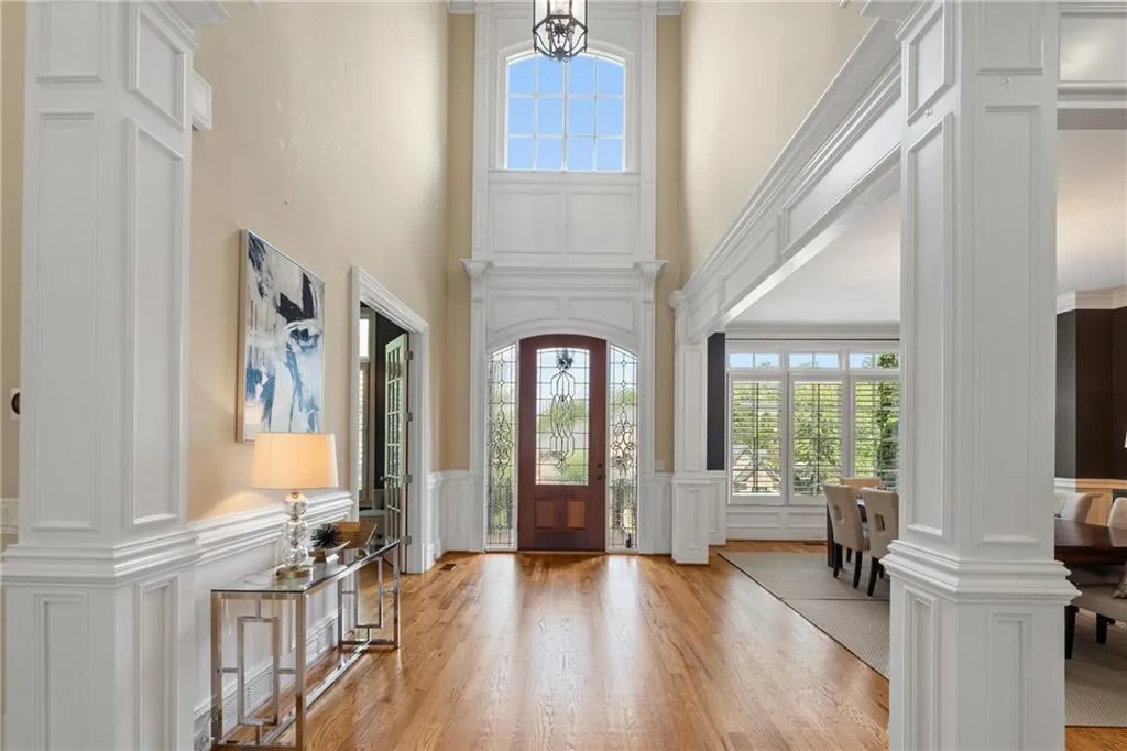 Foyer with a decorative wall, light wood finished floors, ornate columns, a wainscoted wall, and a high ceiling
