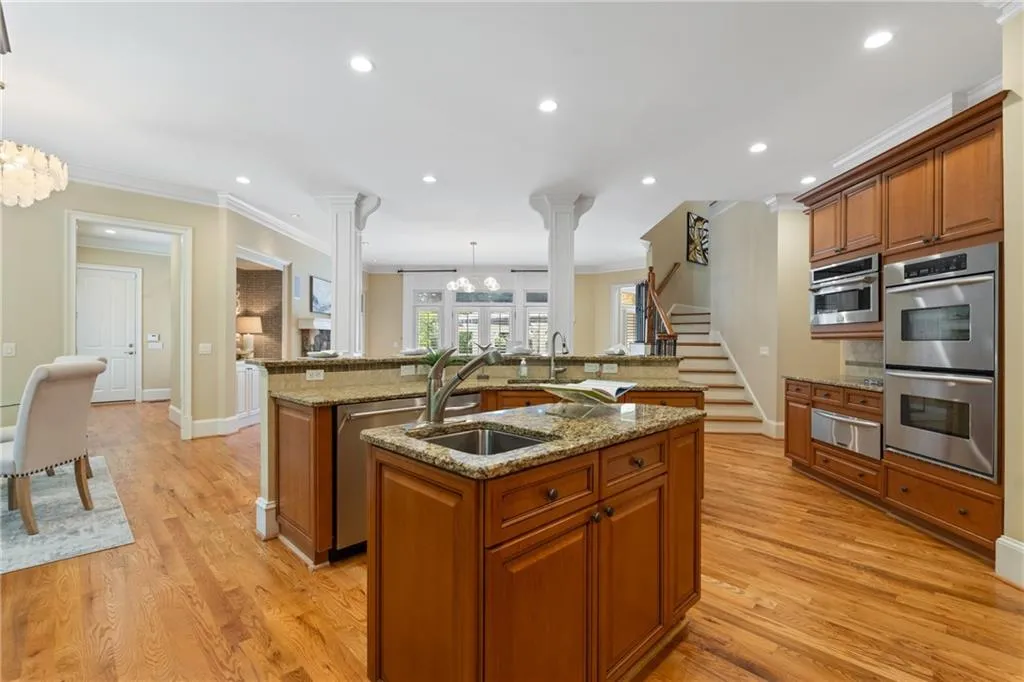 Kitchen featuring a large island, decorative columns, brown cabinetry, appliances with stainless steel finishes, and ornamental molding