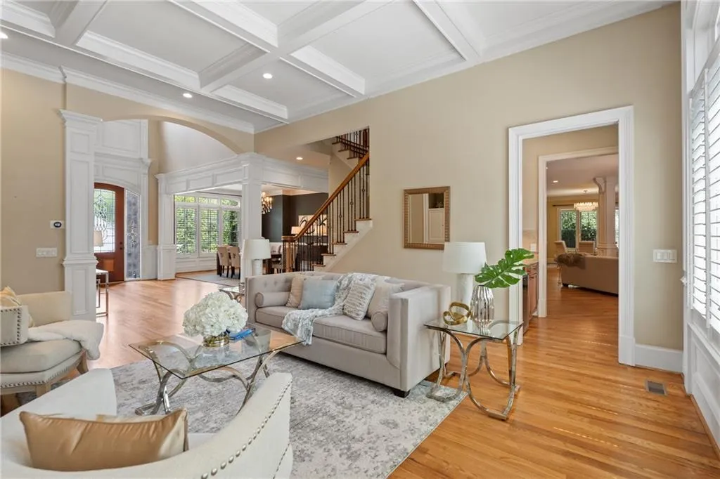 Living room featuring decorative columns, beam ceiling, light wood-style flooring, crown molding, and coffered ceiling