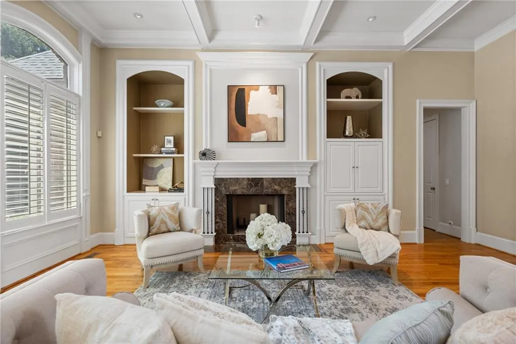 Living room featuring built in shelves, crown molding, wood finished floors, a high end fireplace, and beam ceiling