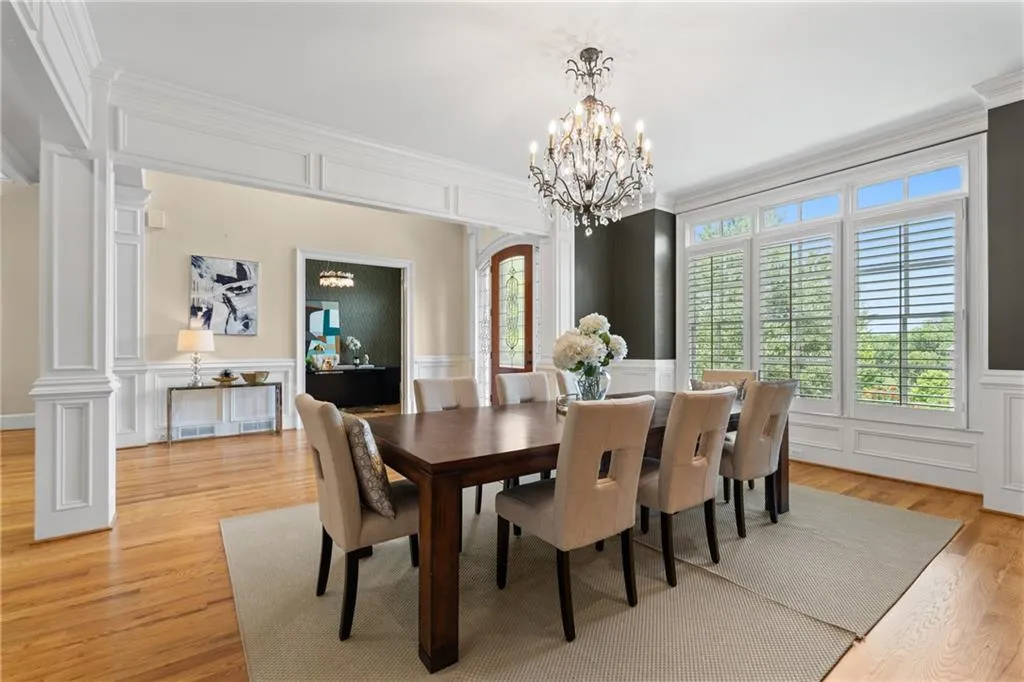 Dining area with a decorative wall, a chandelier, light wood-type flooring, ornamental molding, and wainscoting