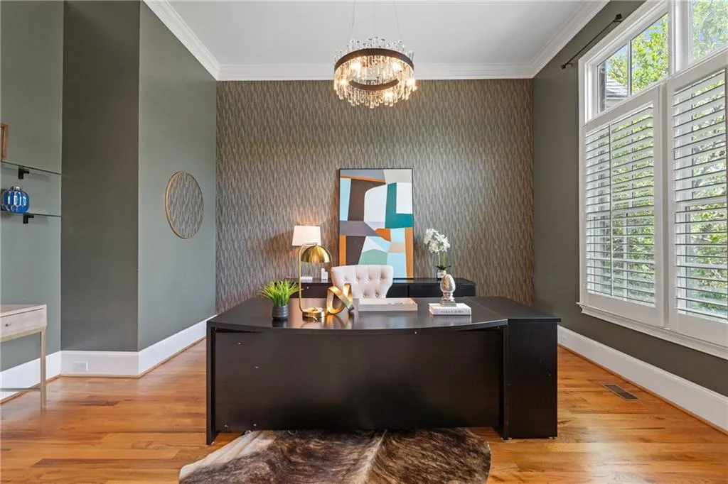Office space featuring a chandelier, healthy amount of natural light, an accent wall, wood finished floors, and ornamental molding