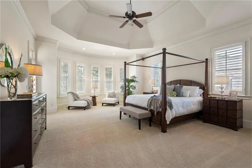 Bedroom featuring a raised ceiling, ornamental molding, light colored carpet, and a ceiling fan