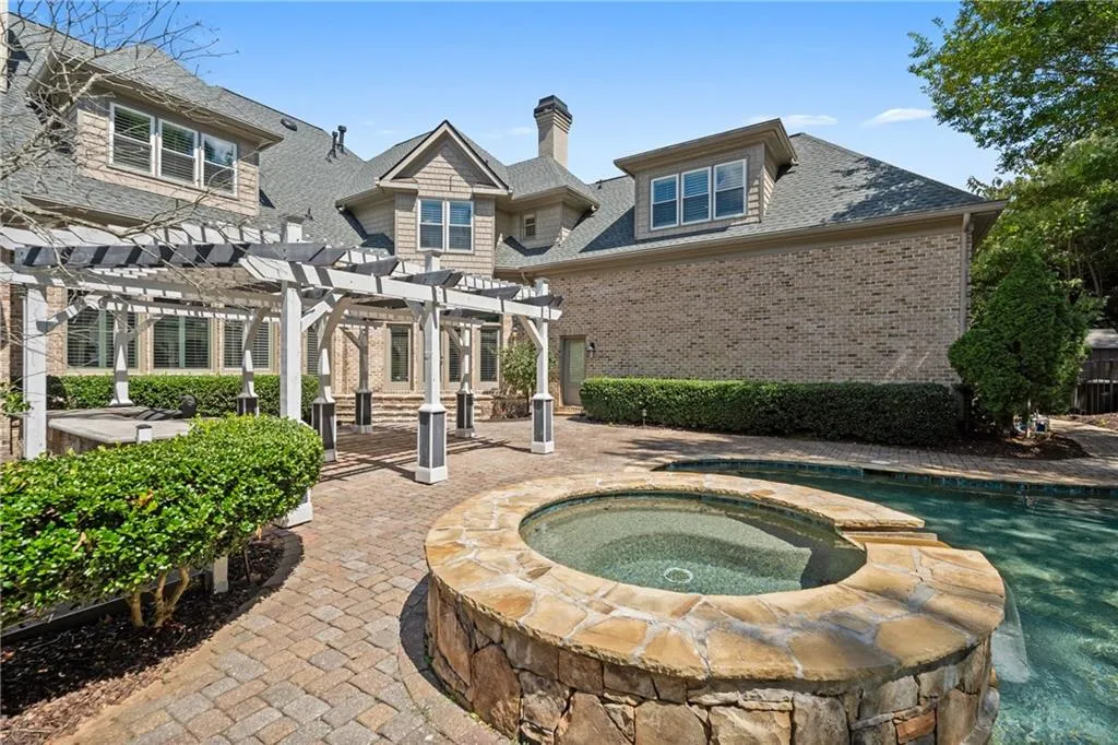 Back of property featuring a pergola, a shingled roof, brick siding, a patio, and a chimney