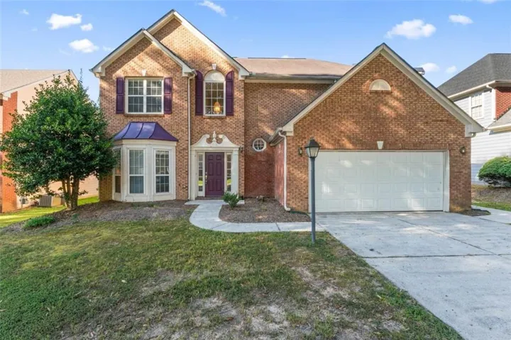 Brick exterior with a gabled roofline, bay window with a metal awning, arched entry, and an integrated two-car garage