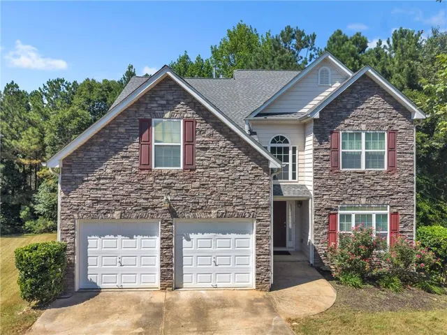 Stone facade exterior with decorative shutters, an arched transom window, a two-car garage, and a concrete driveway