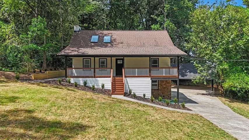 Front exterior featuring a brown roof, two skylights, a covered porch with white railing, and a stone foundation