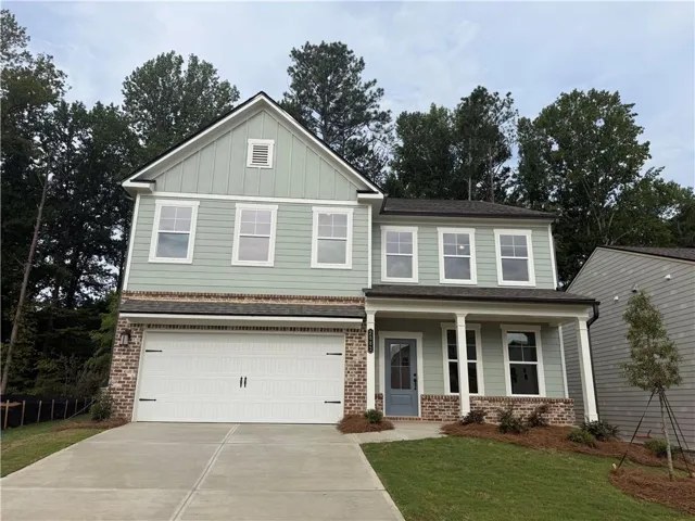 Two-story home with a light green siding, brick accents, white trim, a covered porch, and an attached two-car garage