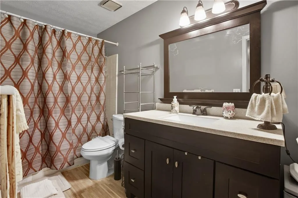 Full bath with vanity, light wood-type flooring, and a textured ceiling
