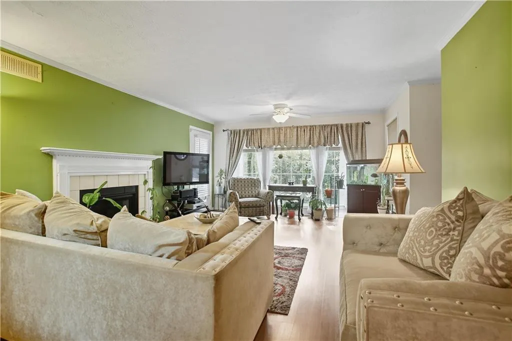 Living room with a fireplace, a ceiling fan, wood finished floors, and crown molding
