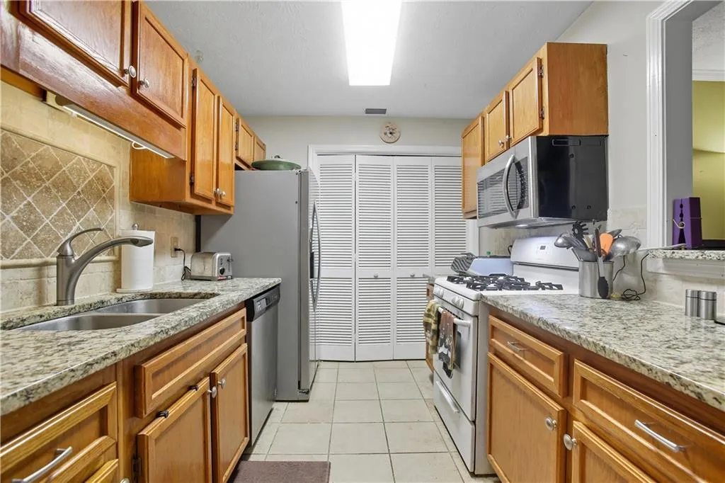Kitchen featuring stainless steel appliances, decorative backsplash, light stone counters, and light tile patterned floors