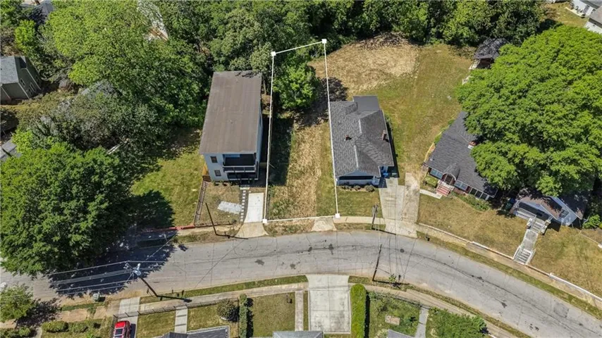 Aerial view of the property, featuring a paved driveway, a green lawn, and surrounding mature trees