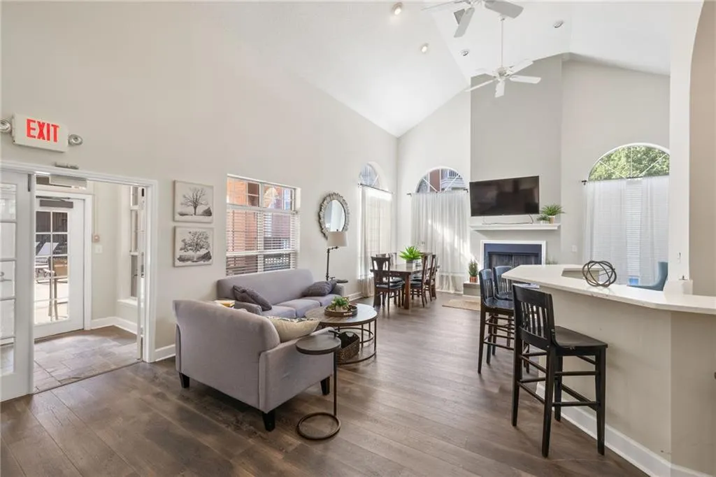 Vaulted ceilings with exposed beams, wood-finish flooring, white fireplace with mantle, and arched windows