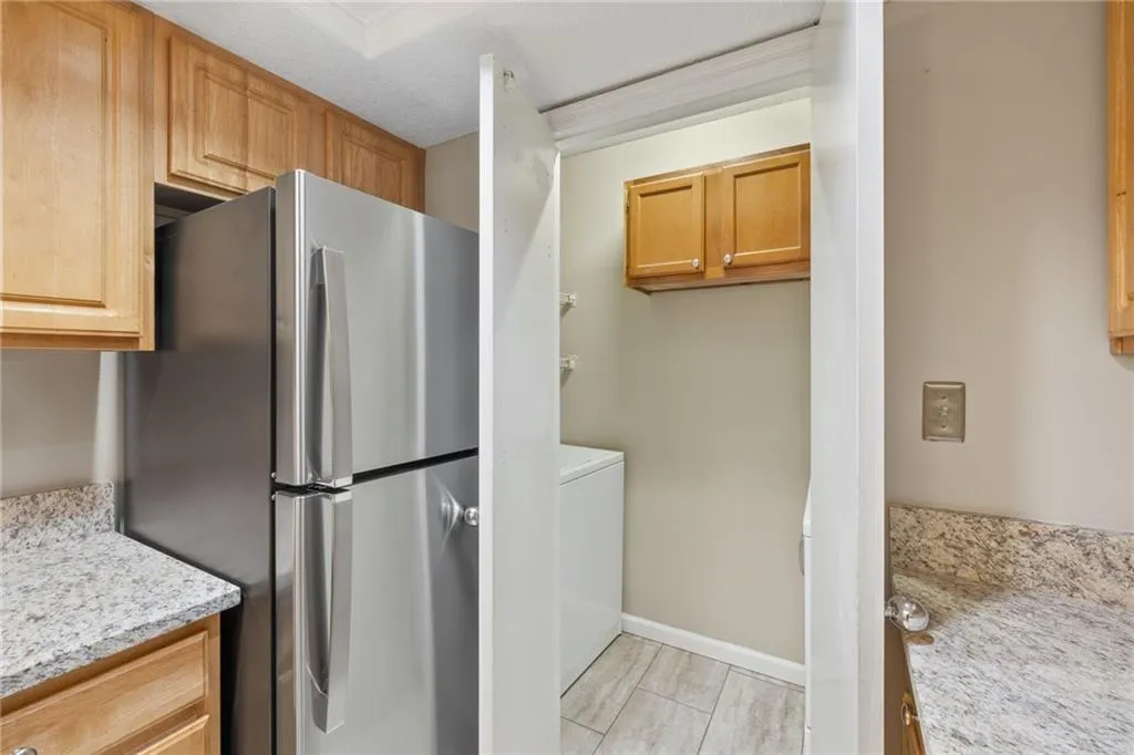 Stainless steel refrigerator, light wood-finish cabinetry, speckled countertops, tile flooring, and integrated laundry area