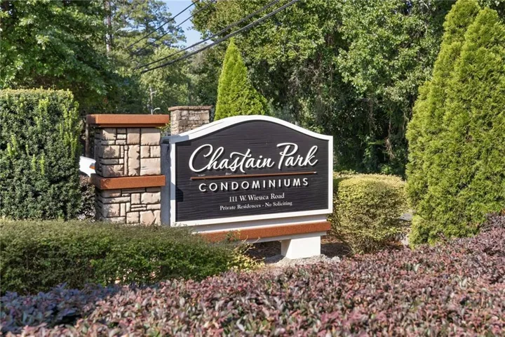 Community entry sign featuring stone pillar accents, dark-paneled signage, and established perimeter landscaping