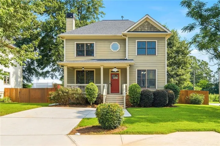 Two-story residence featuring light-colored siding, a covered front porch with white railings, a red entry door, and a prominent octagon window on the second level