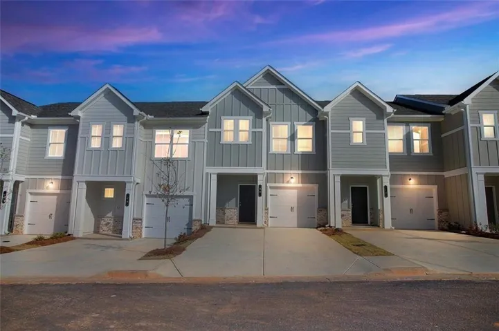 View of front facade with board and batten siding, an attached garage, driveway, and stone siding