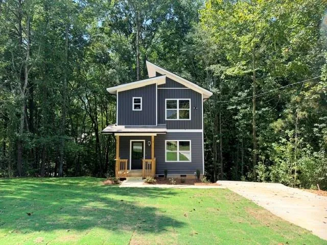 Contemporary architectural style with dark gray siding, a prominent front entrance, a covered porch with natural wood railings, and a concrete driveway