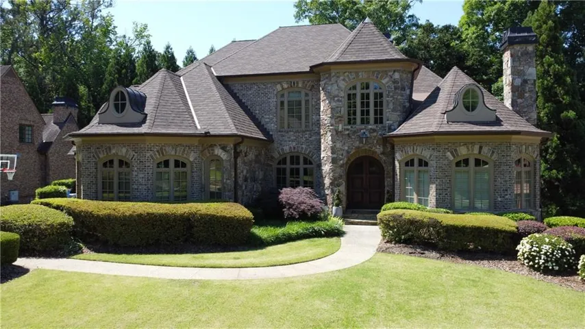 Stone facade residence featuring a prominent front entrance, multiple arched windows, and a shingle roof with dormer details