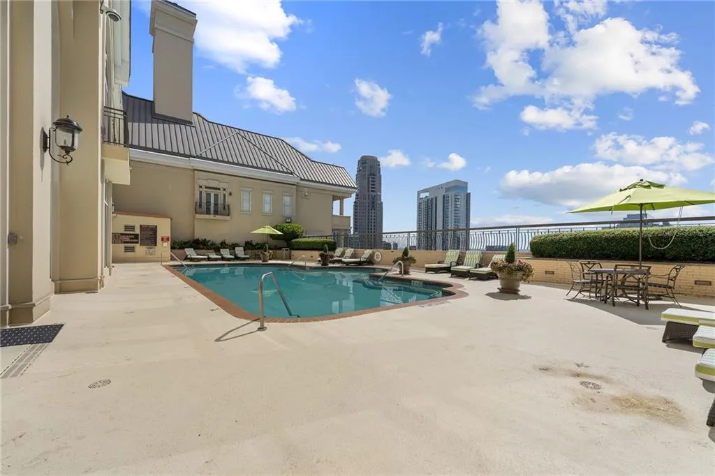 Outdoor pool with surrounding concrete decking, cityscape backdrop, and perimeter landscaping