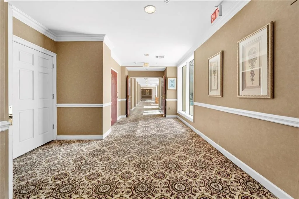 Long hallway featuring patterned carpeting, paneled doors, and wall-mounted picture frames