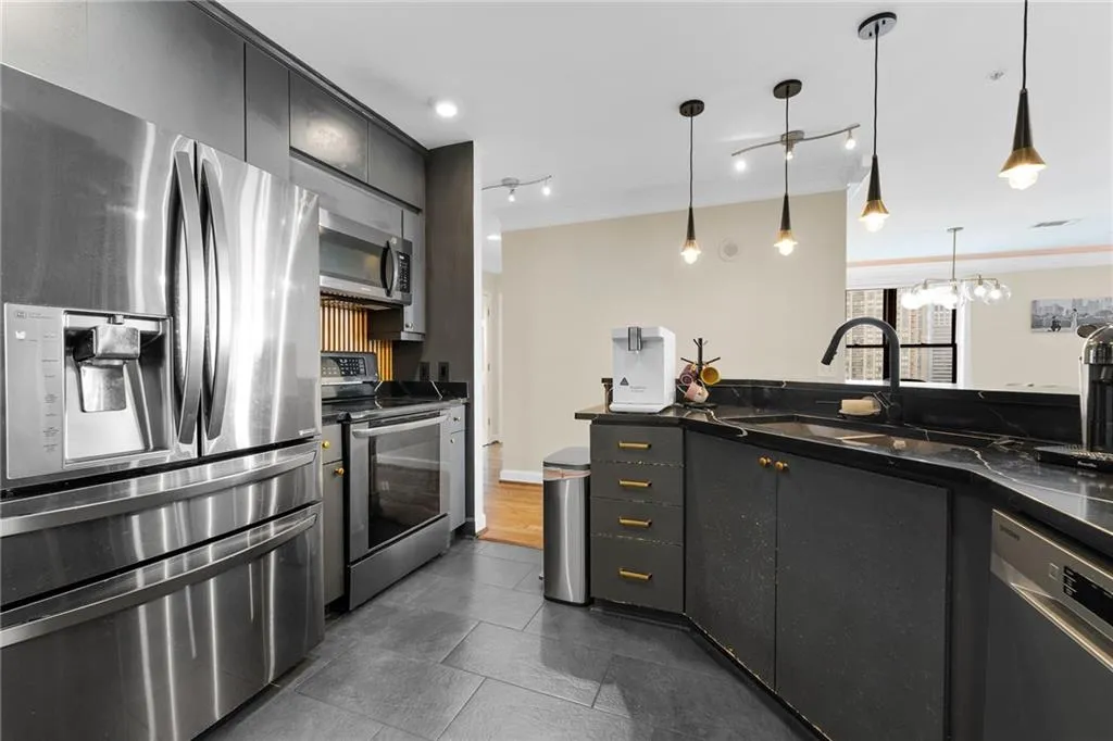 Kitchen featuring stainless steel appliances, dark cabinetry with brass-toned hardware, dark countertop, and tiled flooring
