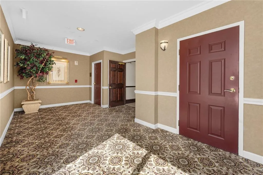 Patterned carpet flooring, chair rail molding, crown molding, paneled entry door, wall sconce lighting