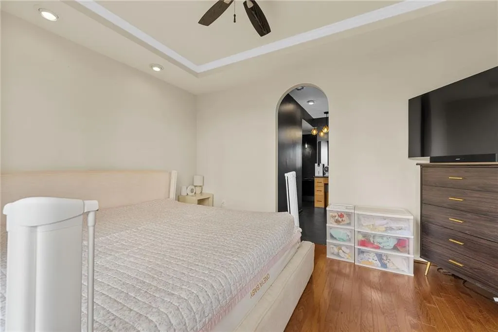 Tray ceiling with recessed lighting and ceiling fan, wood-finish flooring, and an arched doorway