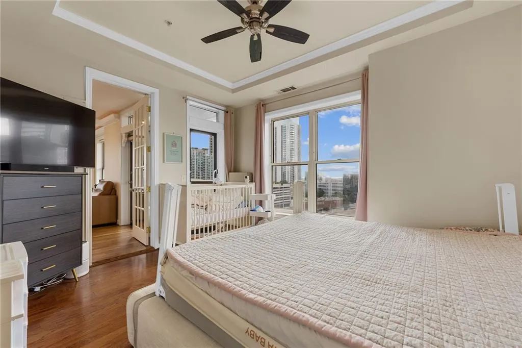 Hardwood-finish flooring, recessed ceiling with crown molding, ceiling fan, and large windows with city scenery