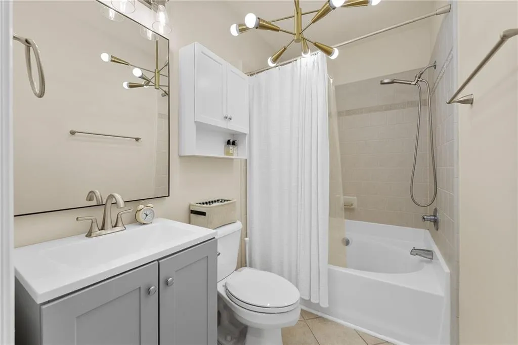 Compact bathroom featuring a white bathtub with tile surround, a vanity with a white countertop and gray cabinetry, a wall-mounted medicine cabinet, and a modern brass light fixture