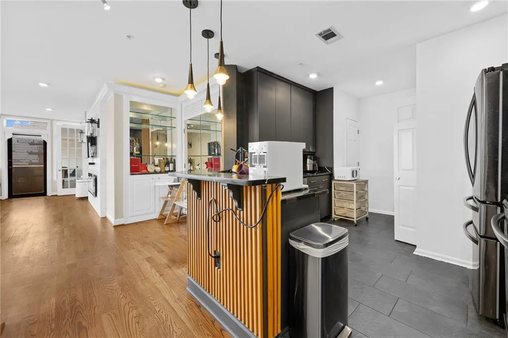 Wood-finish flooring, built-in display cabinetry, stone countertops, pendant lighting, and contemporary dark cabinetry