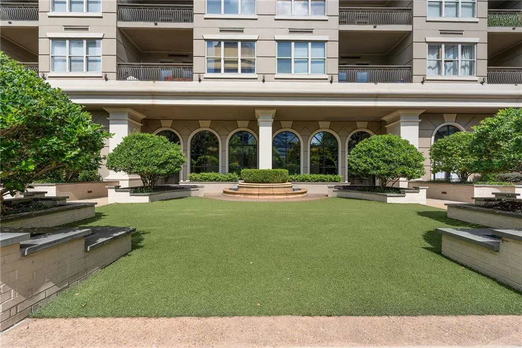 Manicured artificial turf lawn, multi-tiered planter beds, central fountain feature, arched window facade, and columns