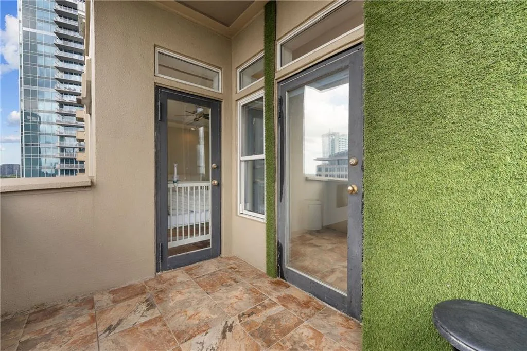Tiled outdoor balcony with artificial turf wall features, glass-paneled doors, and transom windows
