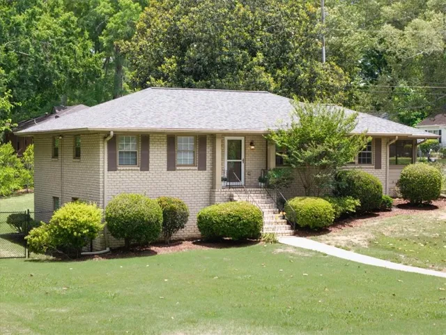 Traditional brick home featuring a gray shingle roof, brown window shutters, and a concrete pathway leading to the front entry