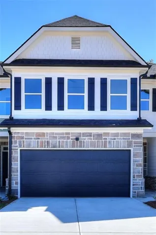 Two-car garage with a textured door, stone veneer facade, white siding, and dark shutters